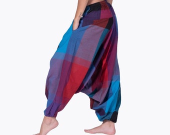 May include: A woman wearing a white t-shirt tied at the waist and colorful plaid pants. The pants have a loose, flowing fit and are gathered at the ankles.