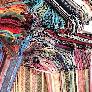 Peut inclure: Une collection de bandes de tissu tissé coloré avec des franges. Le tissu présente une variété de motifs et de couleurs, notamment le rouge, le bleu, le vert, le jaune et le blanc.