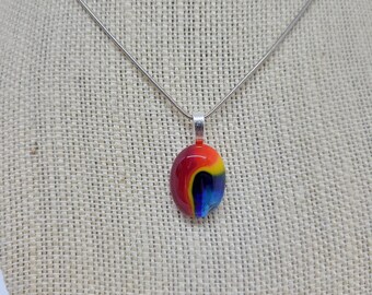 May include: A silver chain necklace with a colorful glass pendant. The pendant is oval shaped and features swirls of red, orange, yellow, blue, and black.