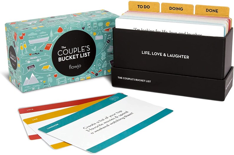 May include: A black box with a teal and white illustrated box lid. The box lid has the text "The Couple's Bucket List" and "flowjo". The box contains a set of cards with the text "Life, Love & Laughter" and "The Couple's Bucket List". The cards are divided into three sections: "To Do", "Doing", and "Done".