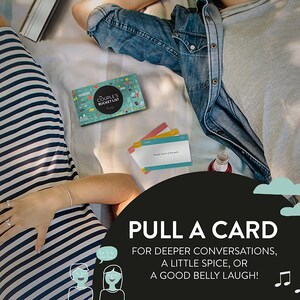 May include: A couple's bucket list card game with a blue, green, and white design. The cards are on a blanket with a couple lying on it. The text on the box reads "The Couple's Bucket List". The text on the card reads "People watch at the park". The text on the bottom of the image reads "PULL A CARD FOR DEEPER CONVERSATIONS, A LITTLE SPICE, OR A GOOD BELLY LAUGH!"