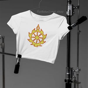 May include: White crop top with a yellow and orange embroidered Dharmachakra symbol. The text "Venkateshwari_shop" is visible on the top of the shirt.