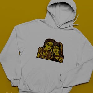 May include: White hoodie with a front pocket and hood. The hoodie features a yellow and black embroidered design of two figures. The text "Venkateshwari_shop" is printed at the bottom. The hoodie is on a yellow background.