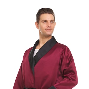 May include: A burgundy satin robe with a black satin trim and a black satin belt. The robe has long sleeves and a shawl collar.