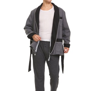 May include: A gray robe with a black satin collar and a white trim. The robe is tied at the waist with a black sash. The person is wearing gray pants.