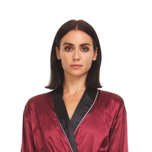 May include: A burgundy satin robe with black lapels and white trim. The robe is made of a smooth, shiny fabric and has a classic design. The model is wearing the robe.