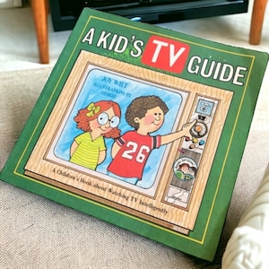 May include: A green book titled "A Kid's TV Guide" with illustrations of children watching television. The book is about watching TV intelligently.