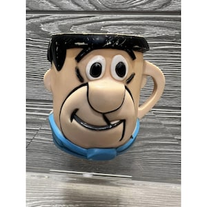 May include: A vintage plastic mug featuring a cartoon character with black hair, a blue shirt, and a big smile. The mug is in good condition with no cracks or chips.
