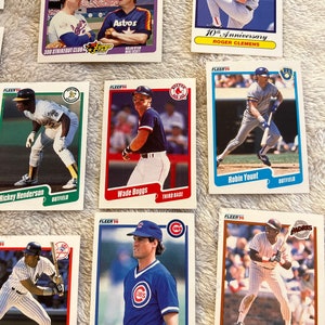 K&ouml;nnte beinhalten: Eine Sammlung von Baseball-Sammelkarten mit Spielern aus den 1990er Jahren. Die Karten stammen aus der Fleer 90-Serie und zeigen Spieler wie Roger Clemens, Wade Boggs, Robin Yount, Tony Gwynn und Ryne Sandberg.