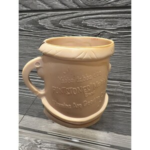 May include: A pink plastic mug with a cartoon image of Fred Flintstone. The mug has a handle and says "Yabba Dabba Doo! Flintstones Multi-Vitamin Brand. Vitamins Are Good to You!"