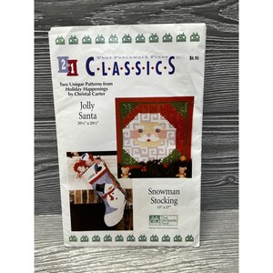 May include: A white paper pattern envelope titled That Patchwork Place 2 for 1 Classics. It features a Jolly Santa quilt pattern measuring 20.5 inches by 20.5 inches and a Snowman Stocking pattern measuring 15 inches by 27 inches by Christal Carter.