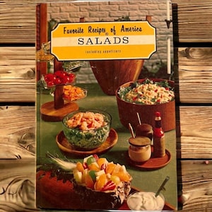 May include: A vintage cookbook titled "Favorite Recipes of America SALADS including appetizers" with a green background and a variety of salads displayed on a table.