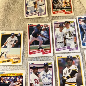 K&ouml;nnte beinhalten: Eine Sammlung von Baseball-Sammelkarten mit verschiedenen Spielern aus den 1990er Jahren. Die Karten stammen aus der Fleer Super Stars-Serie und zeigen Spieler wie George Brett, Kirby Puckett, Don Mattingly und Barry Bonds.