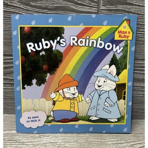 May include: A square children's book titled Ruby's Rainbow featuring Max and Ruby characters in rain gear standing in front of a rainbow. The cover includes a Max & Ruby logo, an apple tree, a white fence, and a cloud graphic stating As seen on Nick Jr.