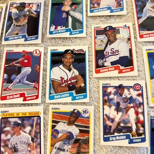 K&ouml;nnte beinhalten: Eine Sammlung von Baseball-Sammelkarten mit verschiedenen Spielern aus verschiedenen Teams. Die Karten stammen aus der Fleer-Serie von 1990 und zeigen Spieler wie Eddie Murray, Larry Walker, Ozzie Smith, David Justice, Sammy Sosa, Greg Maddux, Ken Griffey Jr. und Don Mattingly. Die Karten sind in gutem Zustand und haben einen wei&szlig;en Hintergrund mit blauen und roten Akzenten.