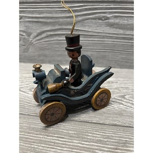 May include: A wooden ornament of a blue car with a man in a top hat driving. The car has gold wheels and the man is wearing a black suit.
