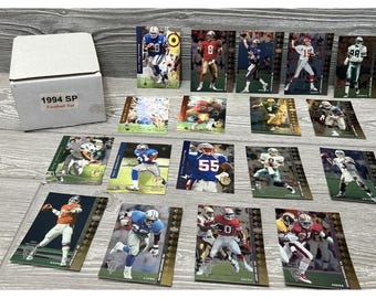 May include: A collection of 1994 SP Football trading cards featuring various NFL players. The cards are in a variety of colours, including gold, silver, and blue. The cards are arranged in rows and columns on a wooden surface. The box in the top left corner reads "1994 SP Football Set".