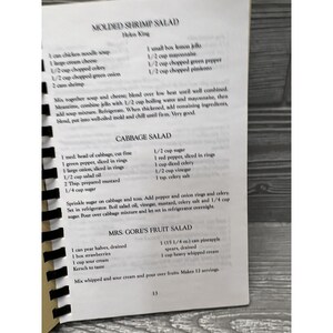 Puede incluir: Un libro de cocina vintage con recetas para ensalada de camarones moldeada, ensalada de col y la ensalada de frutas de la Sra. Gore. Las recetas est&aacute;n escritas a mano e incluyen ingredientes e instrucciones.
