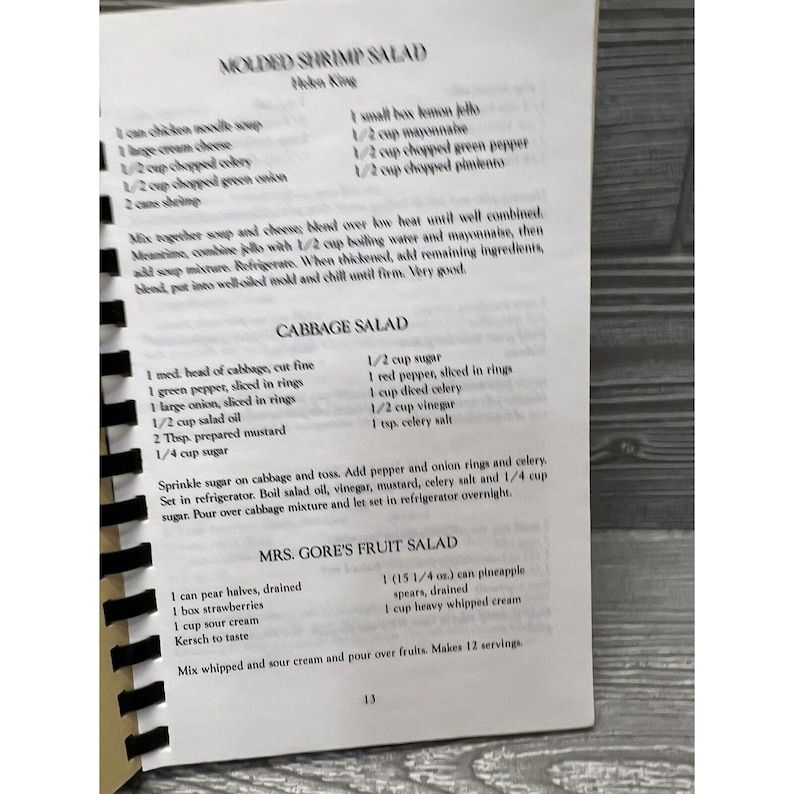 Puede incluir: Un libro de cocina vintage con recetas para ensalada de camarones moldeada, ensalada de col y la ensalada de frutas de la Sra. Gore. Las recetas est&aacute;n escritas a mano e incluyen ingredientes e instrucciones.