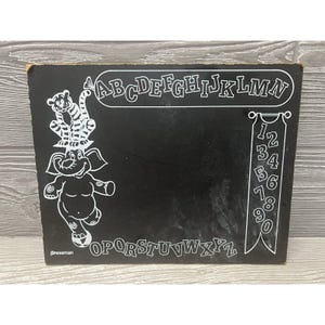 May include: Black chalkboard with white letters and numbers. The letters are in two rows, "ABCDEFGHIJKLMN" and "OPQRSTUVWXYZ". The numbers are in a column, "1234567890". There is a drawing of an elephant with a tiger on its head.