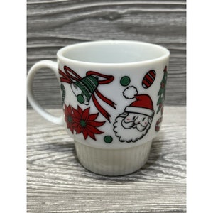 May include: White ceramic mug with a Christmas theme. The mug features a Santa Claus, candy canes, bells, and poinsettias.