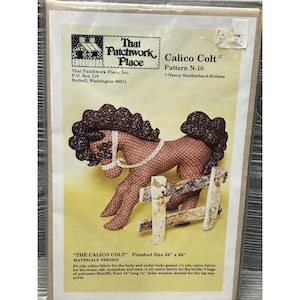 May include: A sewing pattern envelope titled That Patchwork Place Calico Colt Pattern N-10 by Nancy Southerland-Holmes. The cover features a brown and white patterned fabric horse toy standing next to a small wooden fence, with a finished size of 24 inches by 24 inches.