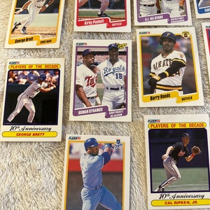 K&ouml;nnte beinhalten: Eine Sammlung von neun Baseball-Sammelkarten mit verschiedenen Spielern aus den 1990er Jahren. Die Karten stammen aus der Fleer 90-Serie und zeigen Spieler wie George Brett, Kirby Puckett, Barry Bonds und Bo Jackson. Die Karten sind in gutem Zustand und haben einen Vintage-Look.
