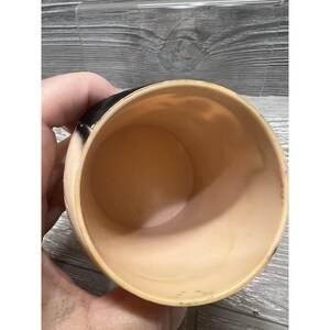May include: A vintage plastic cup with a black and white design. The cup is empty and has a light pink interior.