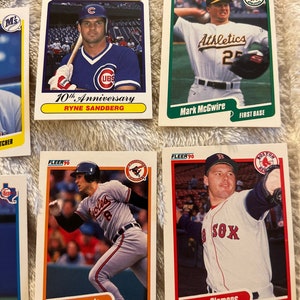 K&ouml;nnte beinhalten: Eine Sammlung von neun Baseball-Sammelkarten mit Spielern aus den 1990er Jahren. Die Karten stammen aus der Fleer 90-Serie und zeigen Spieler wie Ryne Sandberg, Tony Gwynn, Mark McGwire, Cal Ripken Jr. und Roger Clemens. Die Karten sind in gutem Zustand und haben einen wei&szlig;en Hintergrund mit roten, blauen und gr&uuml;nen Akzenten.