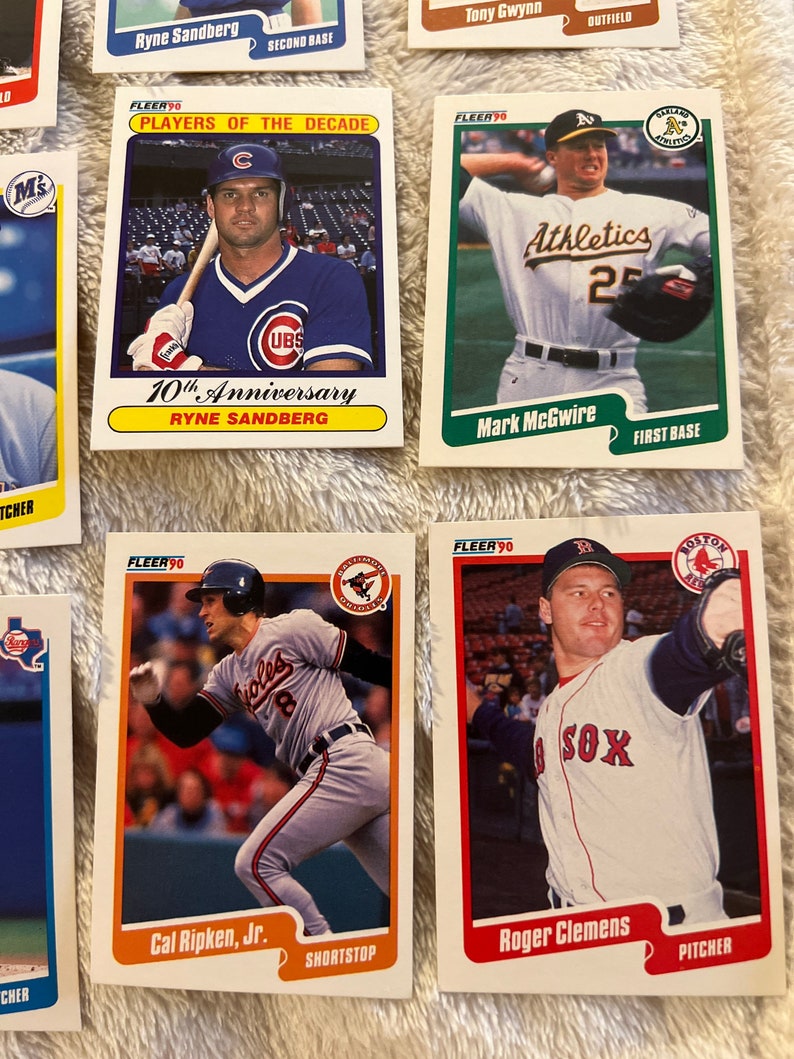 K&ouml;nnte beinhalten: Eine Sammlung von neun Baseball-Sammelkarten mit Spielern aus den 1990er Jahren. Die Karten stammen aus der Fleer 90-Serie und zeigen Spieler wie Ryne Sandberg, Tony Gwynn, Mark McGwire, Cal Ripken Jr. und Roger Clemens. Die Karten sind in gutem Zustand und haben einen wei&szlig;en Hintergrund mit roten, blauen und gr&uuml;nen Akzenten.