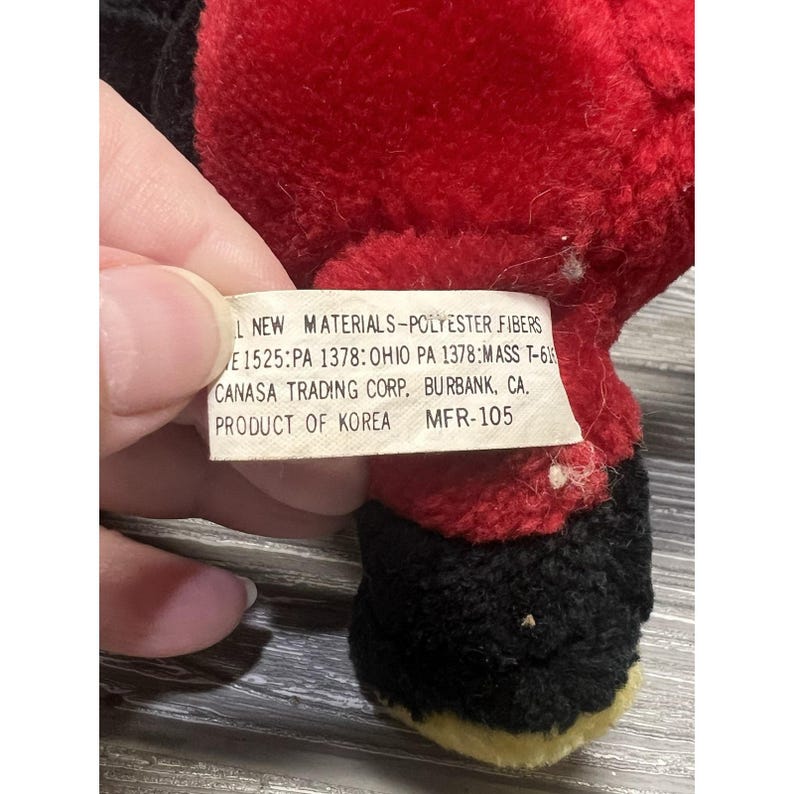May include: A soft toy with red, black, and yellow sections. A label is visible with text including "NEW MATERIALS-POLYESTER FIBERS" and "PRODUCT OF KOREA". The toy's design is partially visible.