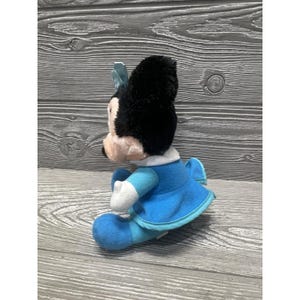 Pode incluir: Uma boneca de pel&uacute;cia da Minnie Mouse, com uma cabe&ccedil;a preta e um la&ccedil;o azul, uma gola branca e um vestido azul. A boneca tem luvas brancas e sapatos azuis. O brinquedo &eacute; feito de tecido macio e &eacute; projetado para crian&ccedil;as.