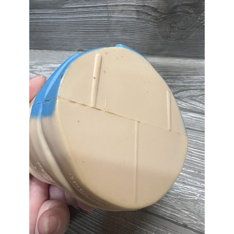 May include: A vintage blue and white plastic toy. The toy is shaped like a person with a round head and a body that is divided into two sections. The toy is made of a hard plastic and has a smooth surface.