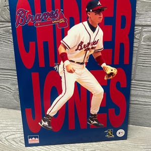 May include: A poster featuring Chipper Jones of the Atlanta Braves in a baseball uniform. The poster has a blue background with the word "Braves" in red, along with the player's name. The player is wearing a white uniform with red and blue accents.