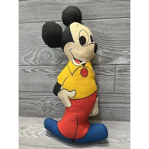 May include: A vintage Mickey Mouse plush toy with a yellow shirt, red pants, and blue shoes. The plush toy is made of fabric and has a smiling face.
