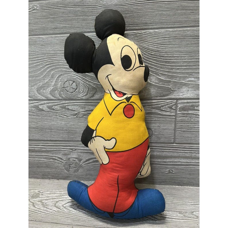 May include: A vintage Mickey Mouse plush toy with a yellow shirt, red pants, and blue shoes. The plush toy is made of fabric and has a smiling face.
