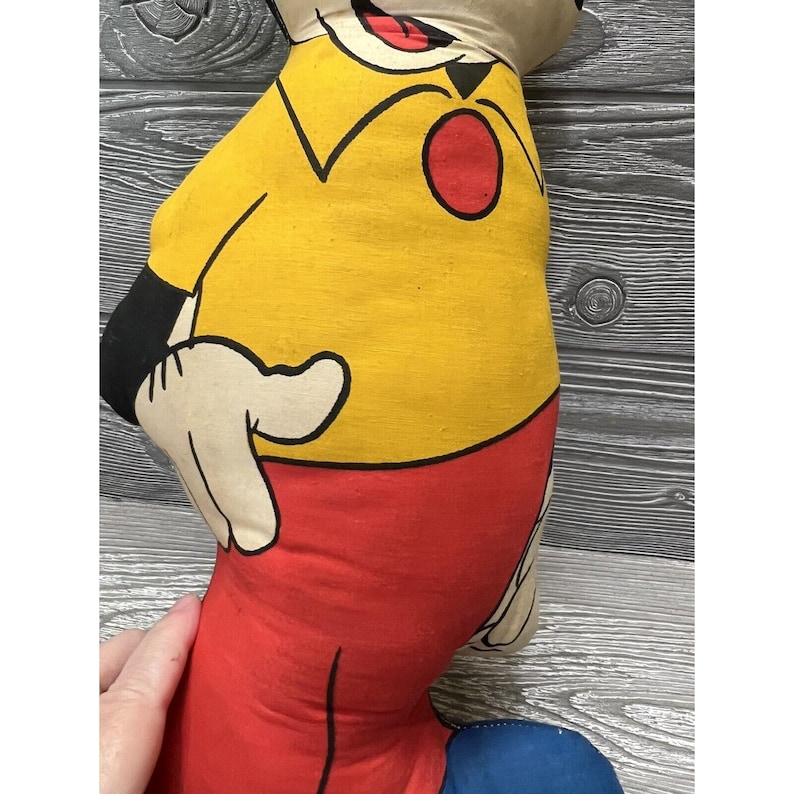 May include: Vintage plush toy of Mickey Mouse. The toy is made of fabric and has a yellow shirt, red pants, and black shoes. The toy is in good condition and has a classic look.