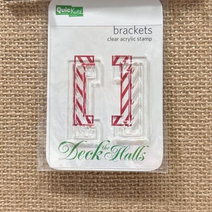 May include: Clear acrylic stamp set with red and white striped brackets. The package reads "brackets clear acrylic stamp" and "Deck the Halls". The stamp set is in a clear plastic package.