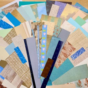 May include: A collection of assorted paper sheets in various sizes and patterns. The papers feature a coastal theme with seashells, starfish, and ocean wave designs in shades of blue, beige, and brown. Ideal for scrapbooking and crafting.