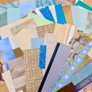 May include: A collection of patterned paper sheets in various colors and textures. Designs include wood grain, marble, woven patterns, and seashell motifs. The assortment features shades of blue, beige, and green, suitable for crafts and scrapbooking.