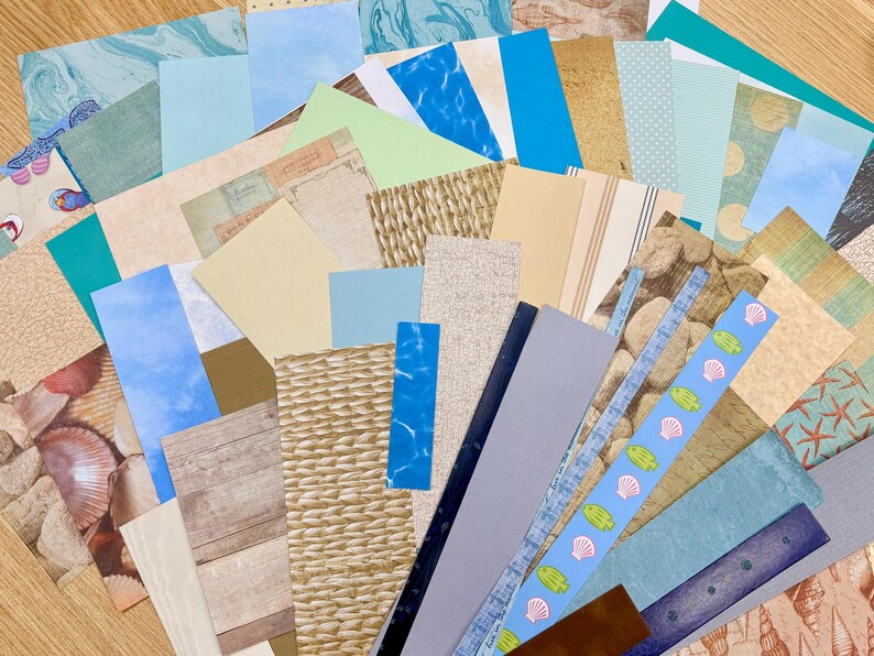 May include: A collection of patterned paper sheets in various colors and textures. Designs include wood grain, marble, woven patterns, and seashell motifs. The assortment features shades of blue, beige, and green, suitable for crafts and scrapbooking.