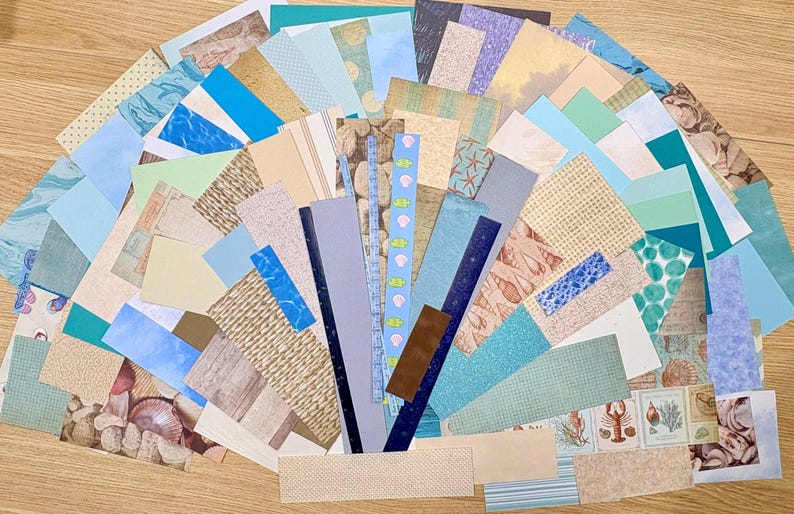 May include: A collection of assorted paper scraps in various shades of blue, green, beige, and brown. The papers feature patterns like seashells, water, and textured designs, ideal for crafting or scrapbooking projects.