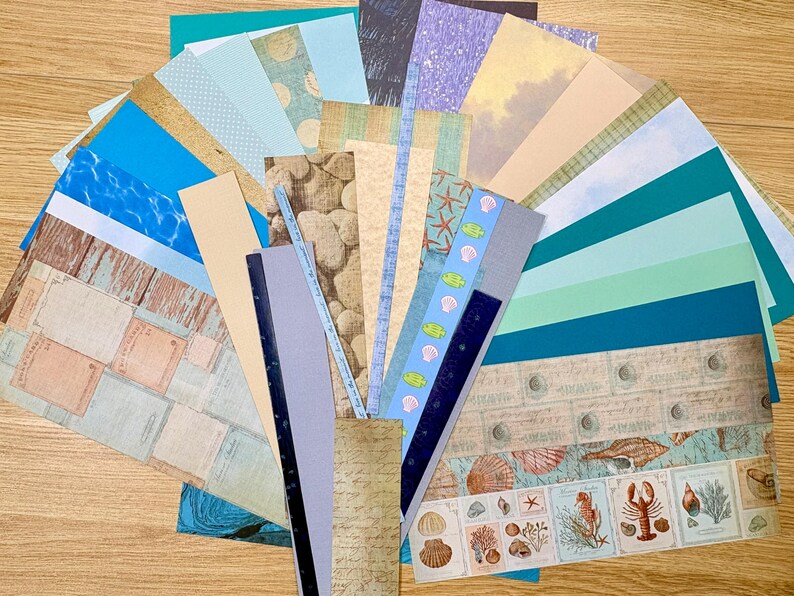 May include: A collection of patterned paper sheets in various colors and designs, including blue water, wood grain, and seashell motifs. The papers are arranged in a fan shape, suitable for scrapbooking or crafting projects.