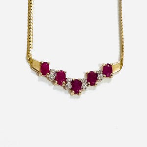 May include: A gold necklace with oval, deep red gemstones and small, clear gemstones. The necklace has a fine gold chain and a curved design. The gemstones are set in a gold setting.