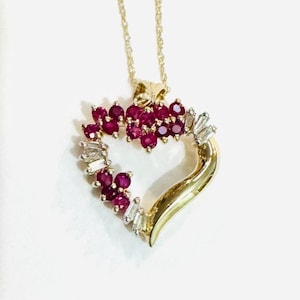 May include: A gold heart-shaped pendant necklace with a ruby and diamond design. The pendant features a swirl design with a cluster of rubies and diamonds around the heart.