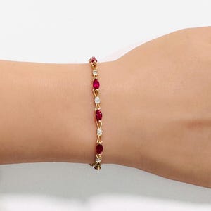 Puede incluir: Una pulsera de oro con un patrón repetitivo de rubíes rojos en talla marquesa y piedras transparentes en talla redonda. Las piedras están engastadas en una delicada cadena de metal dorado, creando un diseño de eslabones continuos.