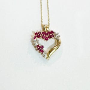 May include: A gold heart-shaped pendant necklace with a cluster of red rubies and smaller diamonds around the edge.
