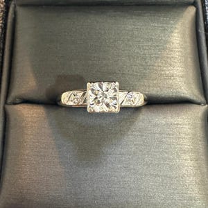 May include: A silver engagement ring with a square-shaped diamond in the center and smaller diamonds on the band.