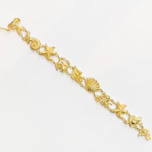 May include: A gold-toned link bracelet featuring a series of interconnected marine-themed charms, including starfish, various seashells, and an octopus, all connected by small circular metal links with a secure clasp at one end of the chain.