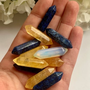 Puede incluir: Una colección de puntas de cristal amarillas y azules. Las puntas están dispuestas en una mano, con las puntas amarillas encima de las puntas azules.